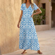 Blue FJØRNA V-neck maxi dress with ruffled hem, flowing fabric, and elegant design perfect for summer or special occasions.