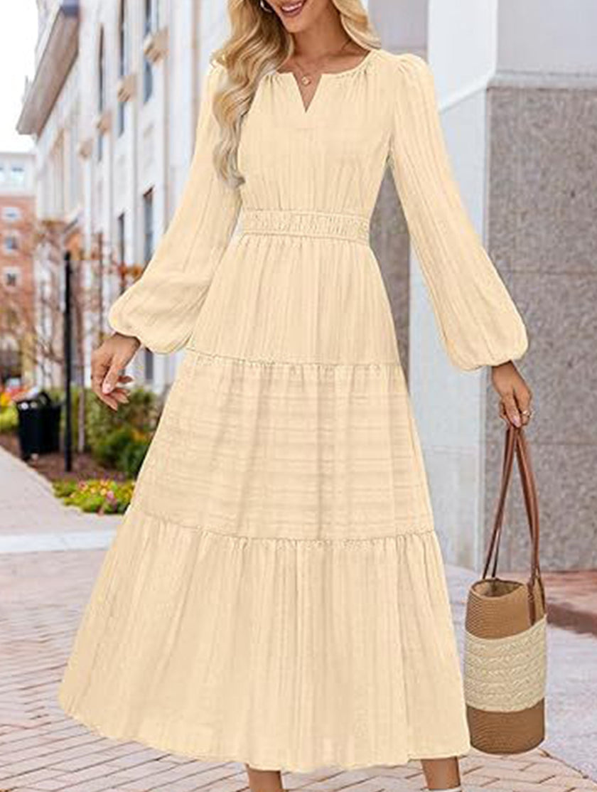 FJØRNA white V-neck pleated waist tiered long-sleeved dress displayed on a mannequin, showcasing elegant design and flowing fabric.