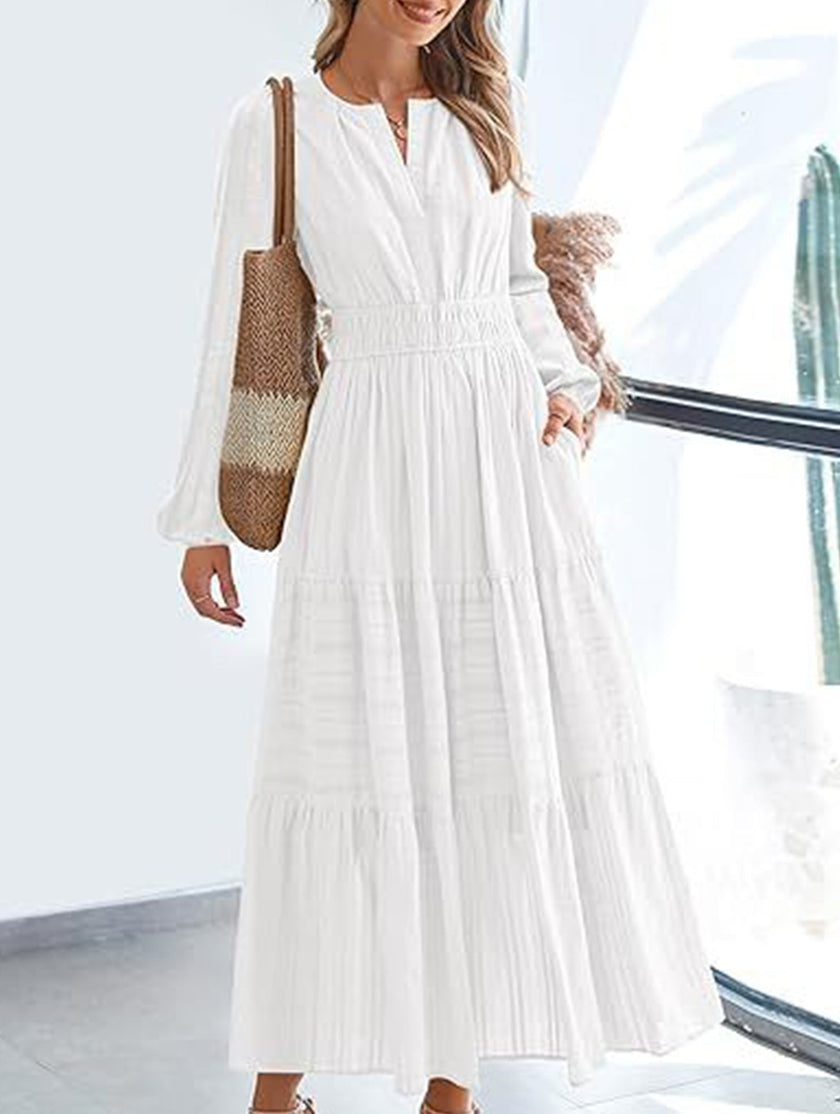 White V-neck pleated waist tiered long-sleeved dress by FJØRNA, showcasing its flowing fabric and elegant silhouette.