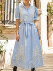 White pastoral style embroidered dress by FJØRNA with openwork details, flowing fabric, and intricate floral embroidery.