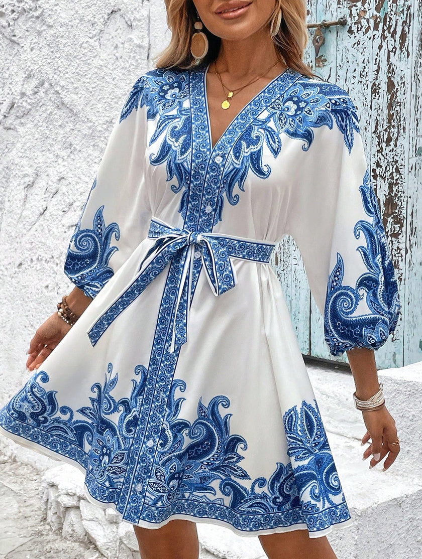 FJØRNA printed white V-neck three-quarter sleeve tie-waist dress displayed on a hanger, showcasing its elegant design and fabric details.