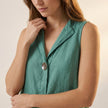 Close-up of FJØRNA women's sleeveless V-neck blouse with statement button details, showcasing fabric texture and stylish design.