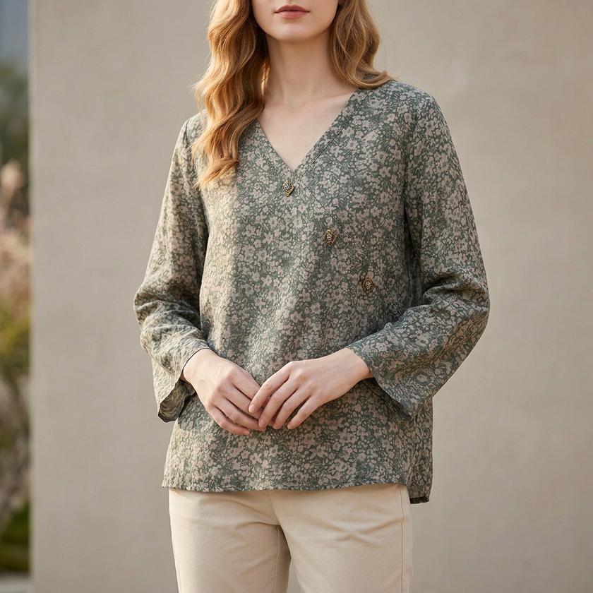 FJØRNA women's summer blouse with V-neck and linen fabric, featuring a slit detail, displayed on a forest-themed background.