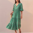 Green FJØRNA midi dress with flowing V-neck, puff sleeves, and tiered skirt, perfect for elegant daytime or evening wear.
