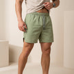 FJØRNA men's quick-dry relaxed-fit green swim shorts with side pockets and slit hem, suitable for beach and pool activities.