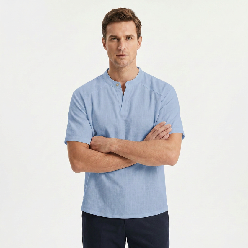 Men's light blue linen short sleeve Henley T-shirt by FJØRNA, shown with crossed arms, casual and breathable summer top.