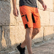 Men’s outdoor performance shorts by FJØRNA with zippered pockets, shown in a casual lifestyle setting.