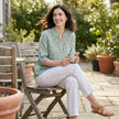 FJØRNA women's summer blouse in denim, flowy style, shown as a casual outfit in a lifestyle setting.