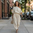 FJØRNA draped one-shoulder top with voluminous lantern pants, stylish resort chic 2-piece set worn in a fashionable lifestyle setting.