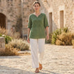 FJØRNA women's floral V-neck linen blouse, flowy summer top worn casually outdoors with greenery in the background.