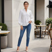 FJØRNA summer women's blouse with v-neck, puff sleeves, and ruffle details, styled as a casual outfit in a lifestyle setting.