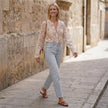FJØRNA women's floral summer blouse with V-neck and lace details, worn casually outdoors with greenery in the background.