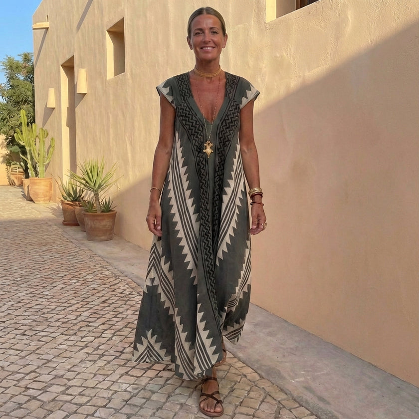 FJØRNA bohemian-inspired flowing A-line maxi dress with deep V-neck and geometric motifs, styled in a relaxed, outdoor setting