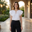 FJØRNA summer blouse for women with cap sleeves and ruffle details, styled in a casual outdoor setting.