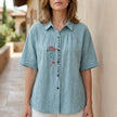 Light blue floral summer blouse for women by FJØRNA, short sleeve denim top with a relaxed fit and feminine design.