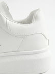 Close-up of FJØRNA men's white lace-up trainers showing minimalist design and detailed stitching on the shoes.