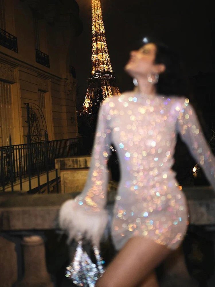 FJØRNA sequin feather mini dress with long sleeves, sheer details, fitted silhouette, and feather cuffs for women’s party wear.
