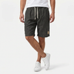 Men's linen shorts by FJØRNA with elastic waist and drawstring, shown from the front with crossed legs on a summer beach style.