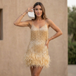 FJØRNA fitted v-neck mini dress with sequined fringe and feathered hem, shown on a model in a stylish indoor setting.