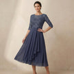FJØRNA embroidered A-line midi dress with sheer sleeves and side pockets, modeled on a woman.