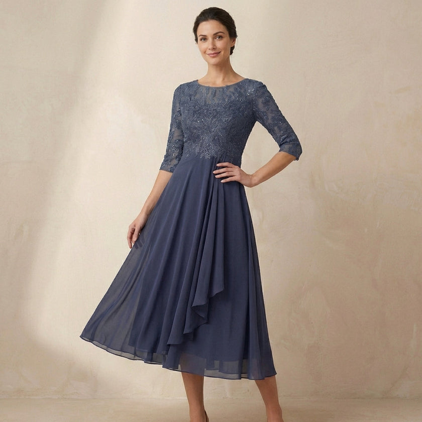 FJØRNA embroidered A-line midi dress with sheer sleeves and side pockets, modeled on a woman.