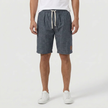 Men's linen shorts by FJØRNA with an elasticated waist and drawstring, worn by a model standing outdoors.