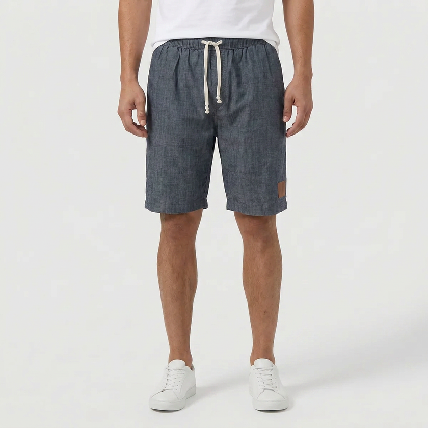 Men's linen shorts by FJØRNA with an elasticated waist and drawstring, worn by a model standing outdoors.