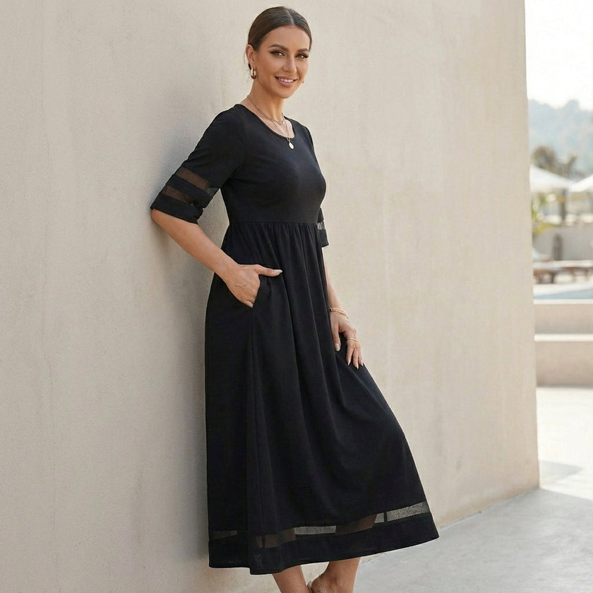 FJØRNA A-line maxi dress with mesh panels and pockets, worn by a model, showcasing its flowing fabric and stylish design.