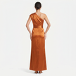 Back view of FJØRNA women's orange one-shoulder maxi evening dress with an asymmetric neckline and flowing silhouette.