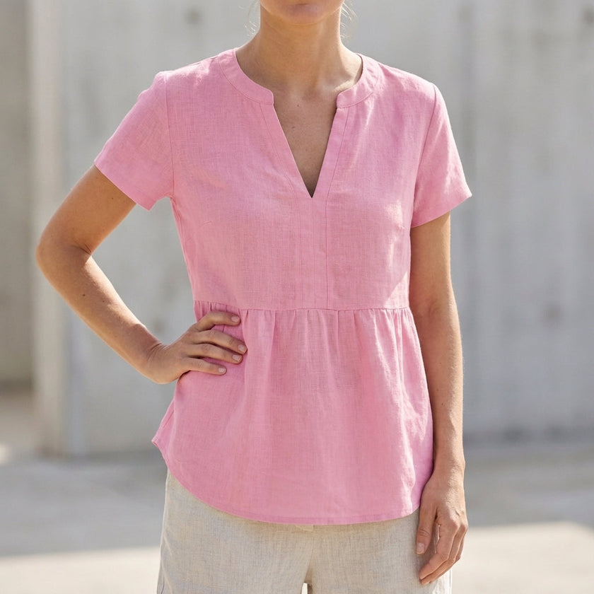 Pink women's V-neck peplum blouse by FJØRNA featuring pintuck detailing and a curved hem, styled on a mannequin.
