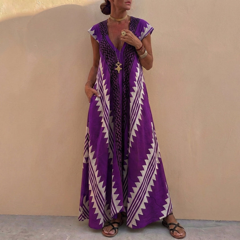 FJØRNA bohemian-inspired purple flowing maxi dress with deep V-neck and geometric motifs, A-line silhouette, lightweight fabric.
