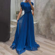 FJØRNA Abigail white pleated evening dress displayed on a mannequin with elegant flowing fabric and V-neck design.
