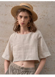 FJØRNA women's linen crop top with short sleeves, lightweight and breathable for casual summer wear, shown in natural fabric detail.