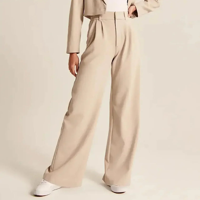 FJØRNA women's wide-leg high-waist trousers showing a flowy, tailored design in neutral fabric, styled for elegant casual wear.