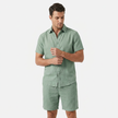 Men's sage green linen short sleeve shirt and shorts two-piece set by FJØRNA, displayed with sleeves adjusted for pose.