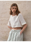 FJØRNA women's linen crop top with short sleeves, lightweight and breathable for casual summer wear, shown in natural fabric detail.