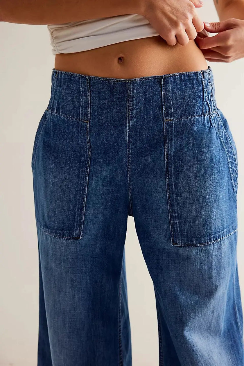 FJØRNA women's wide-leg denim jeans with a relaxed fit, shown hanging on a wooden hanger against a neutral background.