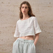 FJØRNA linen crop top for women with short sleeves, lightweight and breathable, shown in a stylish casual setting.