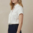 FJØRNA women's summer blouse with short sleeves and cut-out details, shown from the side view in light, breathable fabric.