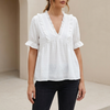 White relaxed peplum blouse with ruffled V-neck and tiered hem, women's FJØRNA top displayed on a hanger.