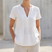 White women's V-neck peplum blouse with pintuck details and curved hem, stylish FJØRNA top perfect for casual or dressy wear.