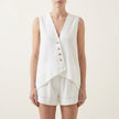 White FJØRNA sleeveless V-neck two-piece set with asymmetrical button-front design on a model.