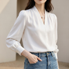 White women's summer blouse with V-neck, puff sleeves, and pleated design by FJØRNA, shown on a hanger.