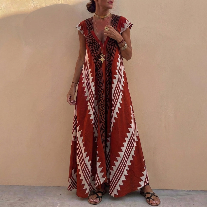 Wine red bohemian-inspired FJØRNA maxi dress with flowing A-line cut, deep V-neck, and geometric motifs, displayed on a hanger.