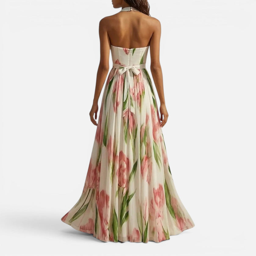 Woman wearing a floral halter maxi dress by FJØRNA, flowing design with vibrant floral pattern perfect for summer or casual wear.
