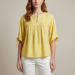 Yellow linen summer blouse for women by FJØRNA, flowing and lightweight, shown on a model with short sleeves and relaxed fit.