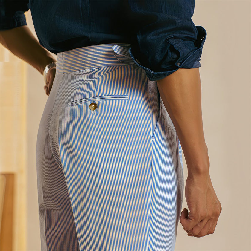 FJØRNA men's high waist straight leg tailored trousers hanging on a wooden hanger, showcasing their classic fit and clean design.