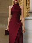FJØRNA burgundy halter-neck asymmetric pleated midi dress displayed on a hanger, showcasing its elegant design and flowing fabric.