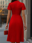 Elegant red pleated midi dress from FJØRNA displayed on a hanger with detailed pleats and a flowing silhouette.