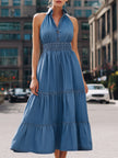 FJØRNA blue halter neck tiered denim maxi dress displayed on a model, showcasing sleeveless design and flowing layered skirt.